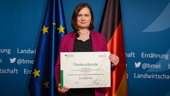Parlamentarische Staatssekretärin Claudia Müller hält die Förderukrund in die Kamera