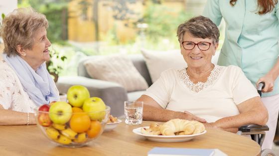 Senioren und eine Betreuungskraft; Auf dem Tisch:Obst und Gebäck