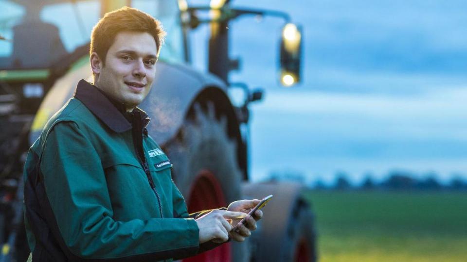 Landwirt mit Smartphone vor Traktor