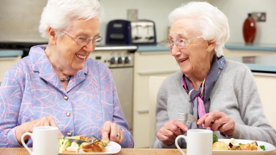 Zwei Seniorinnen sitzen beim Essen am Tisch