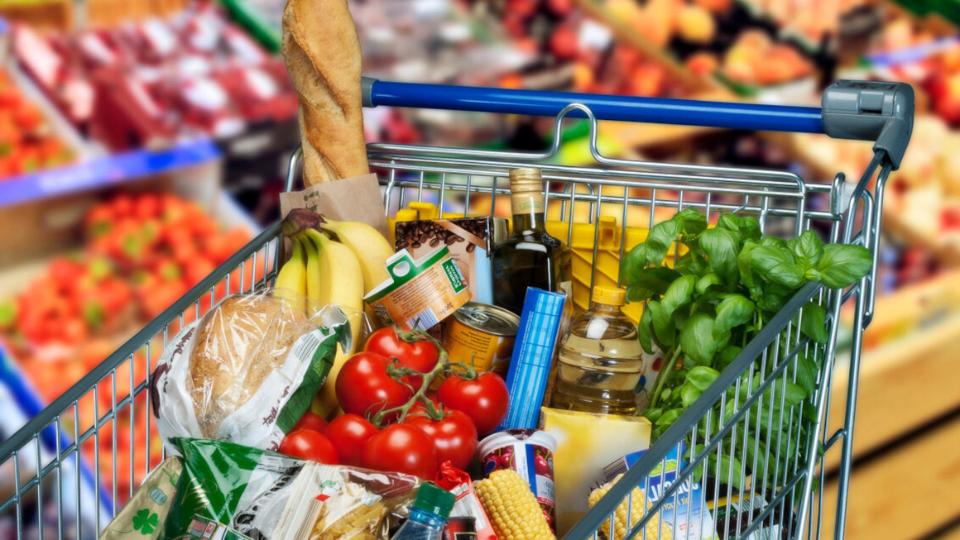 Einkaufswagen gefüllt mich frischen Lebensmitteln wie zum Beispiel: Bananen,Tomaten, Basilikum, Brot, Kaffee in einen Supermarkt