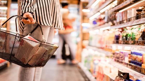 Eine Person steht mit Einkaufskorb vor dem Kühlregal im Supermarkt