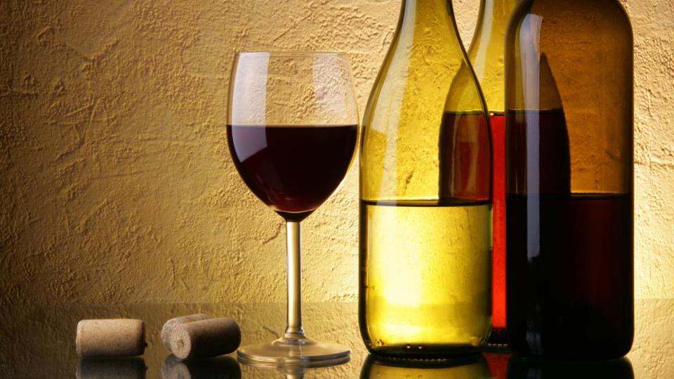 Rotweinglas, daneben drei Weinflaschen