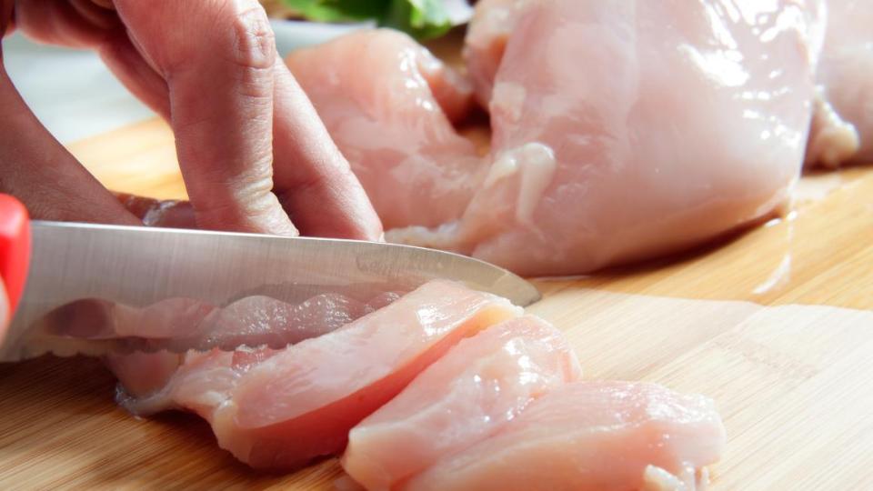 Rohes Hühnerfleisch wird auf einen Brettchen geschnitten