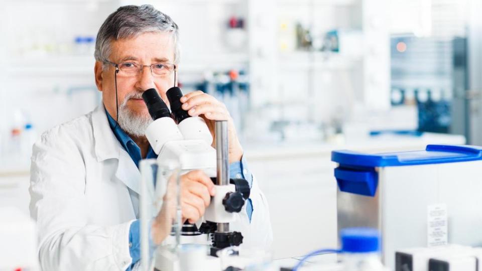 Mann sitzt vor Mikroskop im Labor