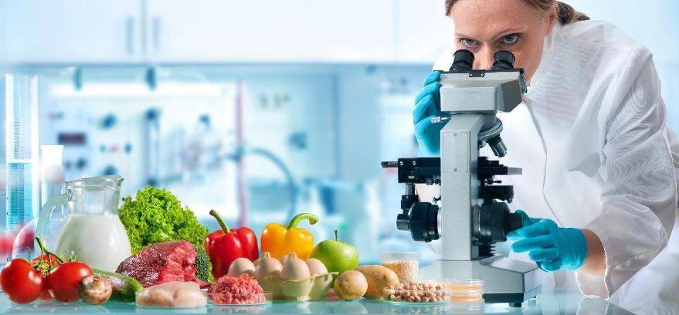 Eine Lebensmitteltechnikerin schaut in einem Labor in ein Mikroskop. Sie prüft Lebensmittel auf Schadstoffe.
