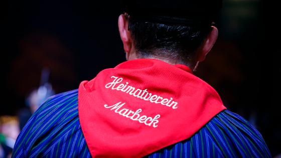Ein Mann von hinten, er trägt ein rotes Halstuch mit der Aufschrift "Heimatverein Marbeck"