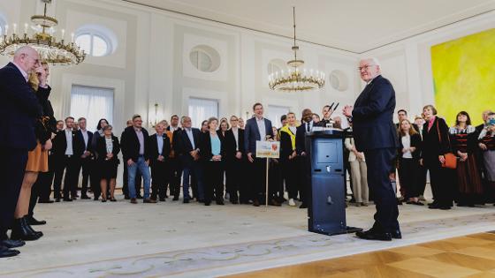 Bundespräsident Bundespräsident Frank-Walter Steinmeier steht am Rednerpult im Kreise der Sieger des Dorfwettbewerbs