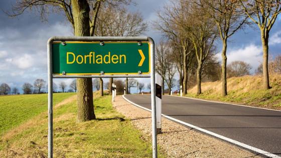 The street sign "Dorfladen" can be seen in front of a country road.